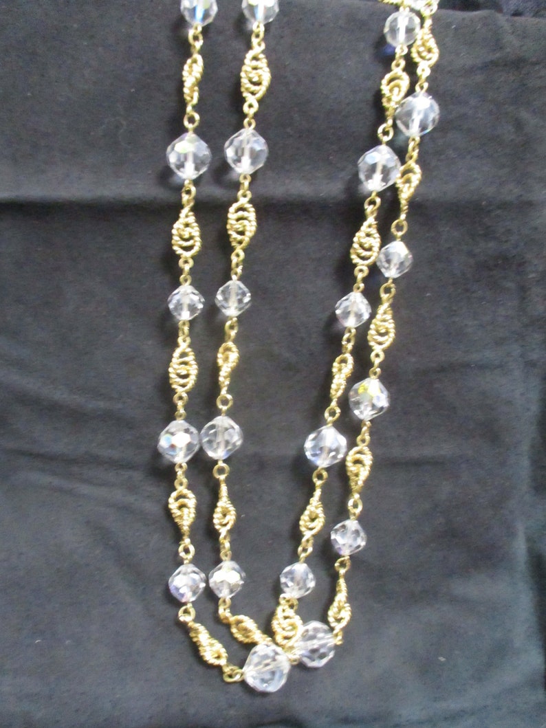 May include: A gold chain necklace with clear crystal beads. The chain is made of twisted gold wire.
