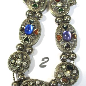 May include: A silver bracelet with oval-shaped charms featuring colorful enamel and rhinestones. The charms are connected by silver beads and a silver chain.