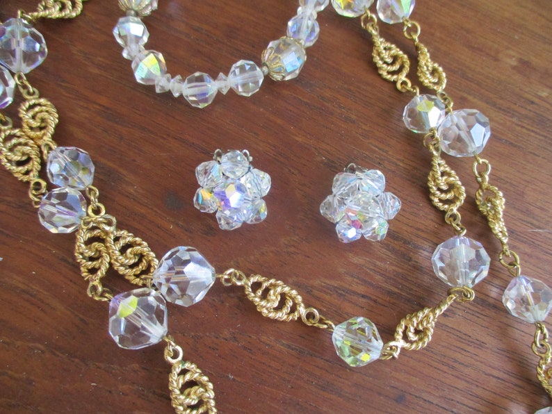 May include: A set of vintage crystal jewelry featuring a long necklace with gold chain and large faceted crystal beads, a shorter necklace with faceted crystal beads, and a pair of crystal earrings.