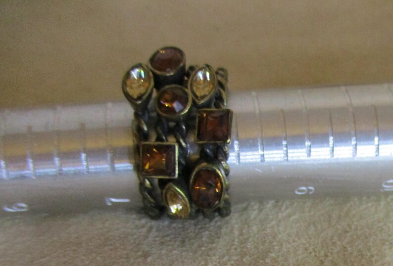 May include: A gold-toned ring with multiple bands adorned with amber and clear faceted stones.