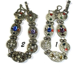 May include: Two silver bracelets with colorful enamel and rhinestone accents. The bracelets have a heart design and are numbered 1 and 2.