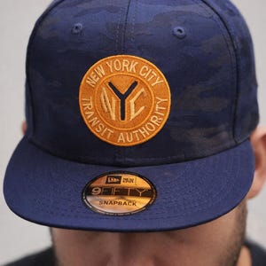 May include: A white ceramic mug with a black handle and the text "But First, Coffee" in a bold, black font. The mug is set against a blurred background, suggesting a cozy setting.