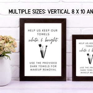 May include: Two framed signs with black frames and white backgrounds. The signs have black and white illustrations of makeup brushes and the text "Help us keep our towels white & bright. Use the provided dark towels for makeup removal."