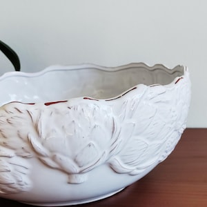 May include: White ceramic bowl with a scalloped rim and embossed floral design. The bowl has a distressed finish with brown accents, adding a vintage aesthetic. Ideal for serving or as a decorative piece.