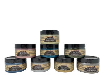May include: Eight jars of Moonshine Metallic paint in various colors, including gold, silver, teal, and green. Each jar has a black lid and a label with the brand name "Moonshine Metallic" and the color name.