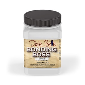 May include: A white plastic bottle with a black lid labelled "Dixie Belle Bonding Boss White 32 fl oz 1946 ml Problem Solver". The label has a brown, textured background and the text is in a black font.