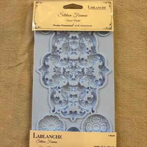 May include: A light blue silicone mold by Lablanche for creating oval ornaments. The packaging features the text Silikon Formen, Silicone Mould, and Ovales Ornament, with dimensions of 12.7 x 20.3 cm printed on the bottom label.