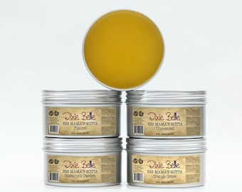 May include: Four silver tins of body butter with labels that read "Dixie Belle Big Mama's Butta" in a vintage font. The scents are Flannel, Unscented, Suzanne's Garden, and Orange Grove.
