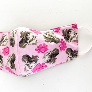 May include: Pink face mask with a pattern of brown dogs and pink flowers.