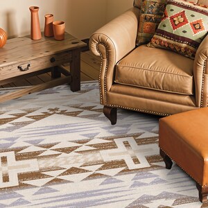 May include: A rectangular area rug featuring a geometric pattern in shades of brown, light blue, and white. The design consists of repeating triangles, horizontal bands, and cross-like shapes arranged in a symmetrical, repeating layout across the surface.
