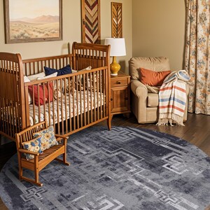 May include: A large, circular area rug featuring a distressed, dark grey and charcoal colour palette with a repeating geometric pattern of light grey, angular, cross-like motifs and linear borders across the entire textured surface.