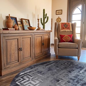 May include: A wooden sideboard with four doors and black hardware, topped with terracotta vessels, framed art, a candle, and a cactus. Beside it sits a beige wingback chair with a red patterned pillow and a small tapestry, atop a dark grey circular rug.