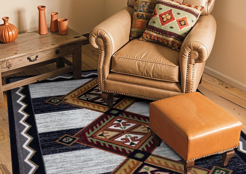 May include: A rectangular area rug featuring a geometric pattern with black, gray, and brown diamond shapes, accented by white zigzag borders. The rug is positioned on a wooden floor beneath a tan leather armchair, a matching ottoman, and a wooden table.