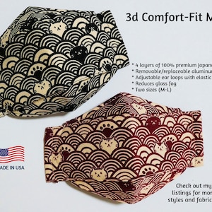 May include: Two 3D comfort-fit face masks with a Japanese-inspired cat and wave pattern. The mask on the left is black and beige, and the mask on the right is red and beige.  The text "3d Comfort-Fit Mask" is at the top of the image. The text "Made in USA" is at the bottom left of the image. The text "4 layers of 100% premium Japanese cotton", "Removable/replaceable aluminum nose piece", "Adjustable ear loops with elastic cord locks", "Reduces glass fog", "Two sizes (M-L)", "Check out my other listings for more mask styles and fabric choices." is at the right side of the image.