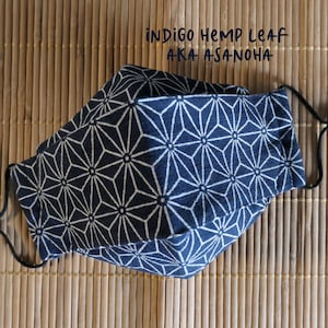 May include: A blue face mask with a white geometric pattern. The mask is made of hemp fabric and has a black elastic band. The text "INDIGO HEMP LEAF AKA ASANOHA" is printed on the mask.