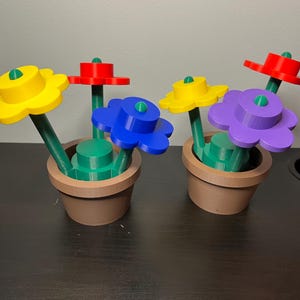 May include: Two colorful flower arrangements in brown pots. The flowers are made of plastic and have different colors, including yellow, red, blue, and purple. The flowers are arranged in a way that they look like they are growing out of the pots.