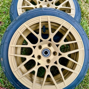 May include: Two gold-colored wheels with black tires. The wheels have a multi-spoke design and are set against a green grassy background. The tires have the text "INFLATE TO 20 P.S.I."
