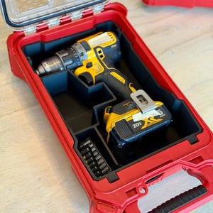 May include: A red, rectangular tool case with a clear lid, housing a yellow and black cordless drill and a black battery pack. The case also contains a set of drill bits. The case is open, revealing the tools inside.