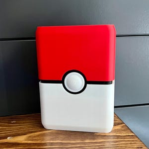 May include: A red and white rectangular container with a black stripe and a white button in the center. The top half is red, and the bottom half is white. The container is sitting on a wooden surface.