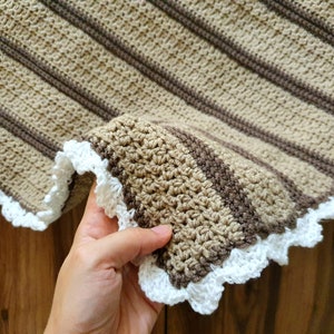 May include: A crocheted blanket with brown and beige stripes and a white crocheted border.