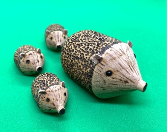 May include: A set of four wooden hedgehog figurines. The largest hedgehog is brown and black with a textured surface. The three smaller hedgehogs are brown and black with smooth surfaces.