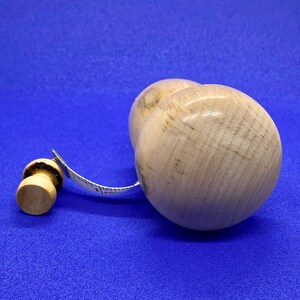 May include: A wooden measuring tape with a light-colored wooden handle and a round, light-colored wooden body. The tape is white with black markings. The background is a solid blue.