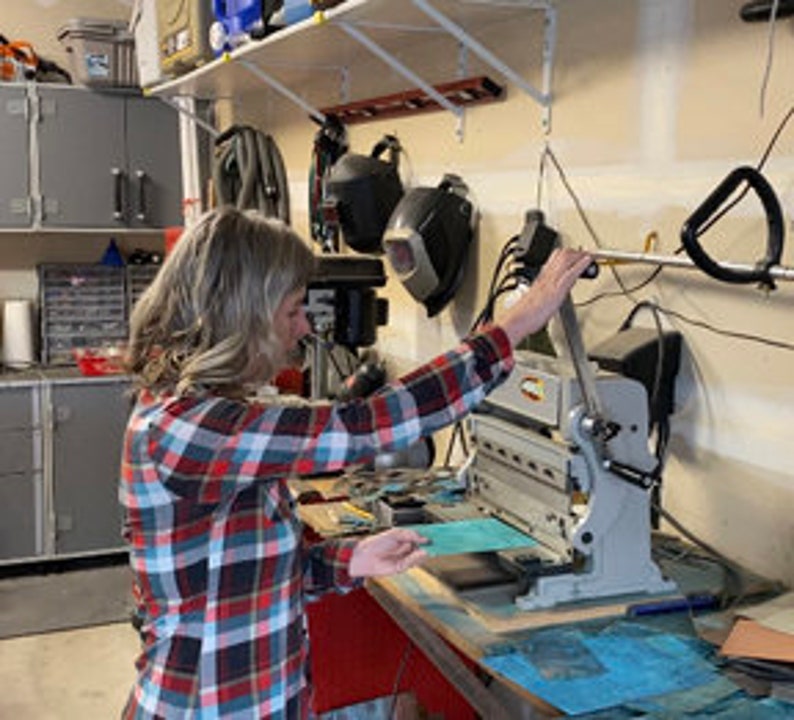May include: A person using a metal paper trimmer to cut a piece of green paper. The trimmer is on a workbench in a garage.