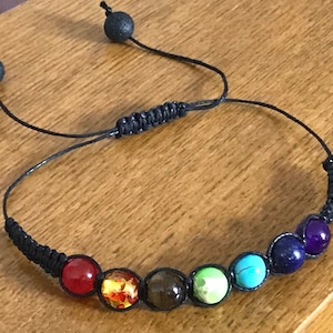 May include: A black string bracelet with seven colorful beads representing the seven chakras. The beads are red, orange, yellow, green, blue, indigo, and violet.