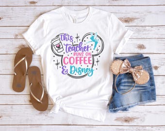 Può includere: Maglietta bianca con un design a forma di testa di Topolino. Il testo sulla maglietta recita "This teacher runs on coffee & Disney".