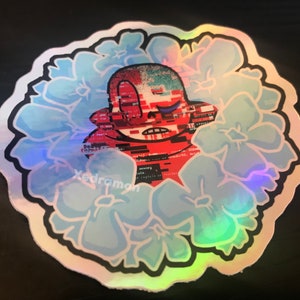 May include: A glittery sticker featuring a red and blue pixelated character with a sad expression surrounded by light blue flowers. The character has a skull-like face and is surrounded by code-like text. The text "Xedraman" is visible at the bottom of the sticker.