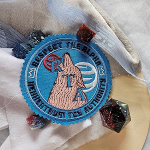 May include: A blue embroidered patch with the text "Respect the Alpha Hierarchy" and a pink wolf howling at the moon.