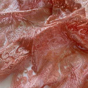 May include: Peach-coloured embroidered tulle fabric with a delicate floral pattern. The fabric is sheer and has a soft, flowing texture.