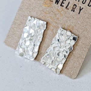 May include: A pair of silver earrings with a textured, hammered finish. The earrings are rectangular in shape and are displayed on a card with the text "Danielle Robichaud Jewelry".