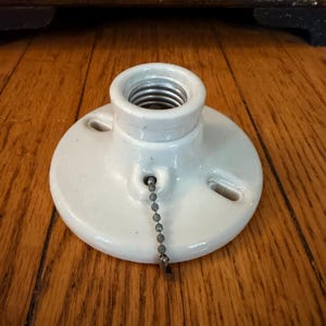 以下が含まれることがあります： 2つの取り付けスロットを備えた円形のベースと、中央に金属製のネジ山を持つ白いセラミック製の電球ソケット。ソケットの前面には、手動でライトを操作するための銀色の金属製プルチェーンがぶら下がっています。