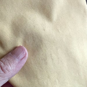 May include: Close-up of a light yellow fabric with a fine weave. The fabric has a smooth, slightly textured surface.