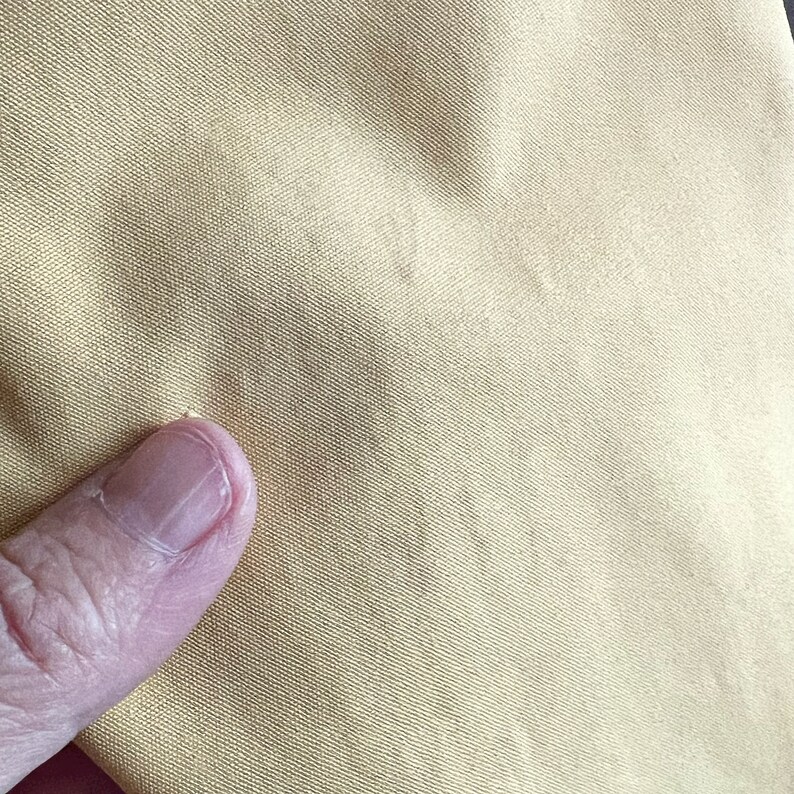 May include: Close-up of a light yellow fabric with a fine weave. The fabric has a smooth, slightly textured surface.