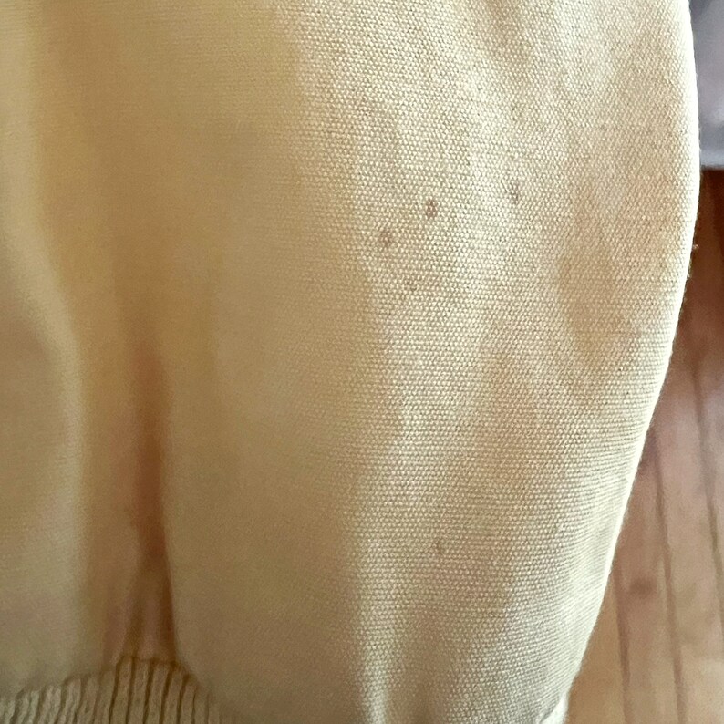 May include: A close-up of a light yellow knitted fabric with a subtle texture. The fabric has a few small brown spots.