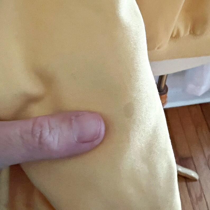 May include: Close-up of a pale yellow satin fabric with a slight sheen. The fabric is smooth and wrinkle-free.