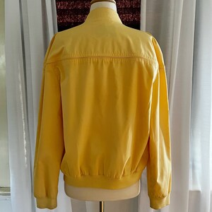 May include: A yellow bomber jacket with a ribbed collar and cuffs. The jacket has a zipper closure and two pockets.