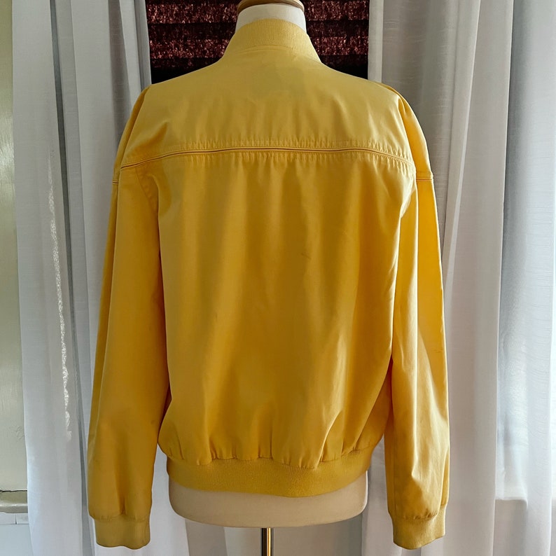 May include: A yellow bomber jacket with a ribbed collar and cuffs. The jacket has a zipper closure and two pockets.