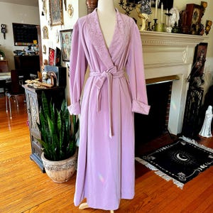 Peut inclure: Une longue robe de couleur lavande avec un col en dentelle et une ceinture à nouer assortie. La robe est faite d'un tissu doux et moelleux.