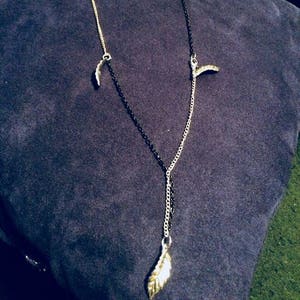 Puede incluir: Un collar de plata con una cadena negra y varios colgantes de hojas de plata. El collar está sobre un fondo de tela azul.