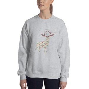 May include: A gray sweatshirt with a patterned reindeer design. The reindeer is made up of snowflakes and stars in shades of red, blue, and beige. The reindeer is surrounded by a scattering of snowflakes.