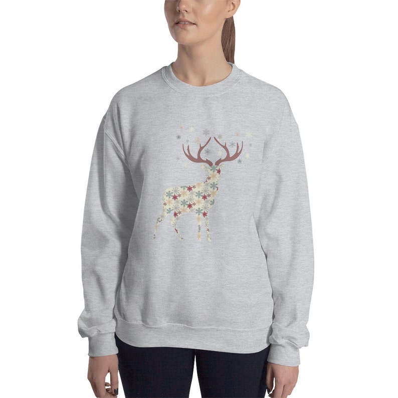 May include: A gray sweatshirt with a patterned reindeer design. The reindeer is made up of snowflakes and stars in shades of red, blue, and beige. The reindeer is surrounded by a scattering of snowflakes.