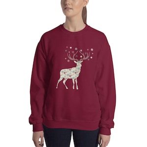 May include: A maroon sweatshirt with a white silhouette of a deer with snowflake patterned antlers. The deer is surrounded by small snowflakes.