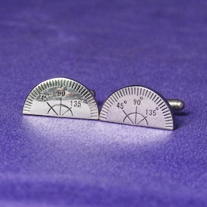 May include: A pair of silver cufflinks shaped like protractors with the numbers 45, 90, and 135 degrees printed on them.