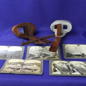 May include: Two antique wooden stereoscopes with a set of vintage stereoscopic cards. The stereoscopes are made of wood and have a metal frame. The cards are black and white and feature images of people and landscapes.