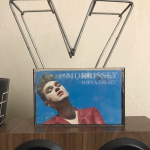 May include: A cassette tape with a blue background and a photo of Morrissey on the front. The cassette tape is titled "Morrissey" and "Bona Drag" in white text.