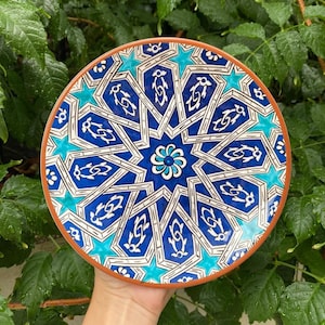 May include: A blue and white ceramic plate with a geometric pattern. The plate has a brown rim and is decorated with a starburst design.