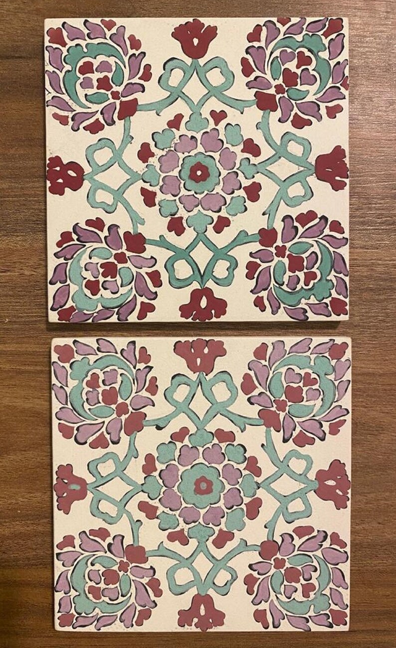 May include: Two square ceramic tiles with a white background and a repeating floral pattern in shades of red, purple, and green. The pattern features stylized flowers and leaves.